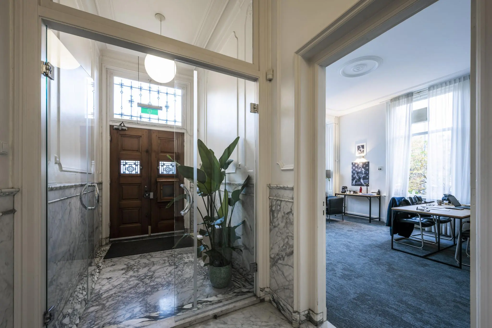 Entreehal met marmeren vloer en houten deur, met zicht op een modern ingericht kantoor aan de Van Eedenstraat.